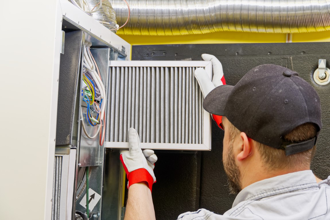 Technician examining the front grill of an external wall mounted heating and cooling unit